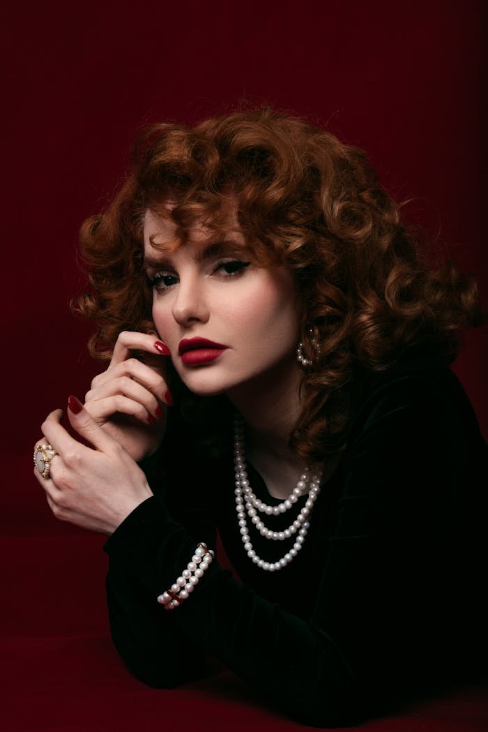 Home Elegant vintage-style portrait featuring a woman in pearls on a rich maroon backdrop.