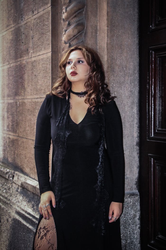 Home Woman in gothic attire standing against stone wall, conveying elegance and mystery.